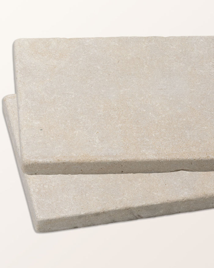 Two Castilan Limestone Cobbles Tumbled tiles stacked at an angle against a plain background, showing the tumbled edge and the pale honeyed surface