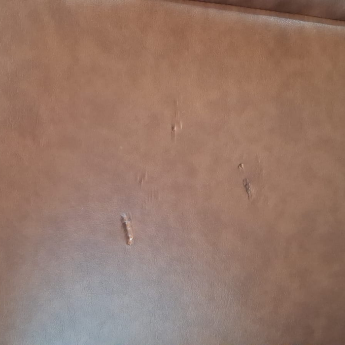 A close-up of a brown faux leather or leather material surface with a few small scratches and scuffs visible.